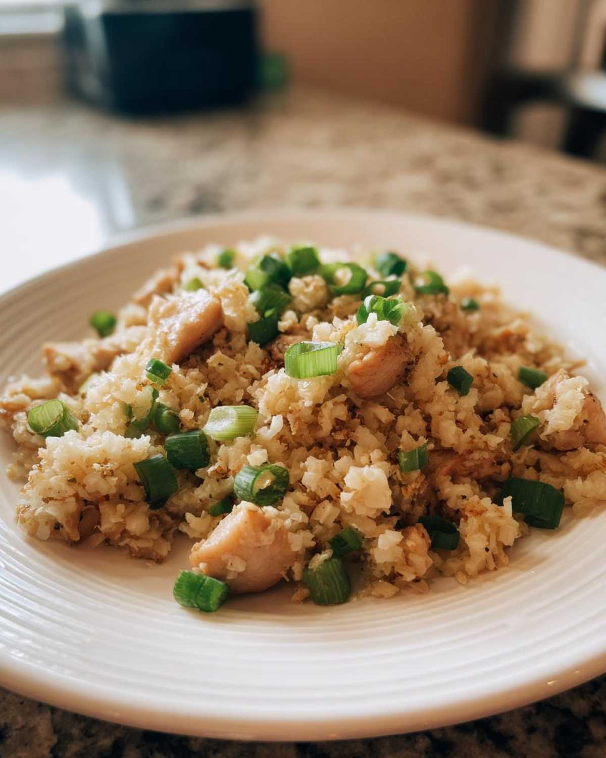 A close-up of chicken cauliflower fried rice topped with fresh green onions, served on a white plate.