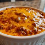 Close-up of hot, bubbly chili cheese dip topped with melted, bright orange cheddar cheese in a white ramekin.