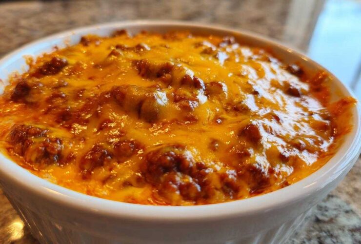 Close-up of hot, bubbly chili cheese dip topped with melted, bright orange cheddar cheese in a white ramekin.