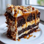 A decadent slice of chocolate caramel toffee crunch cake layered with dark chocolate cake, cream, and dripping with caramel sauce.