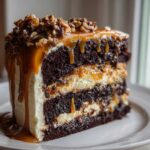 A decadent slice of chocolate caramel toffee crunch cake featuring dark layers, white frosting, and dripping caramel sauce with nuts.