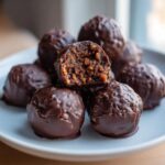 A stack of chocolate-covered pecan pie balls, with one cut in half showing the textured, nutty interior.