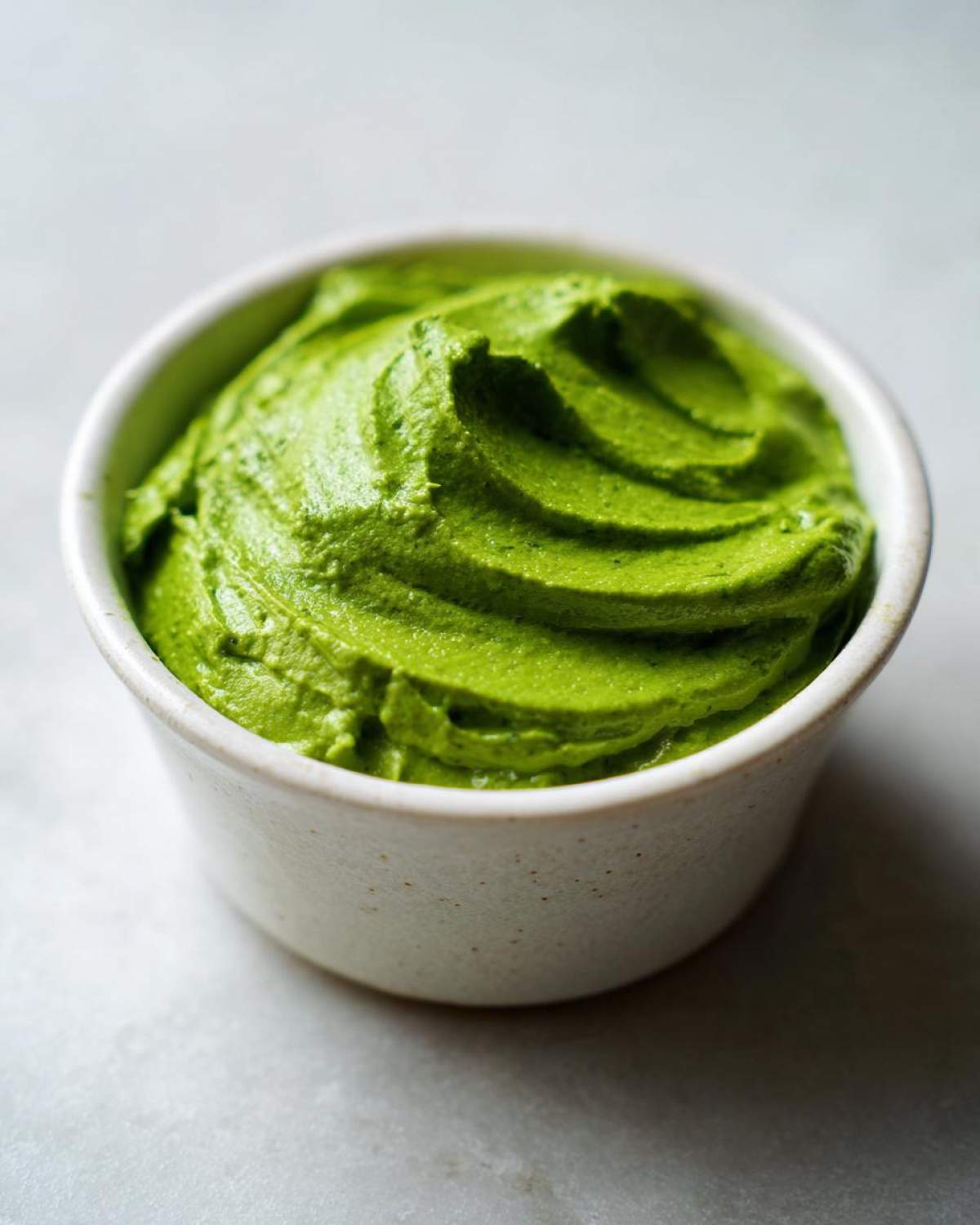 Close-up of thick, vibrant green cilantro lime sauce swirled in a small white ceramic bowl.
