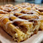 Close-up of a soft, gooey slice of cinnamon roll apple pie topped with white icing.