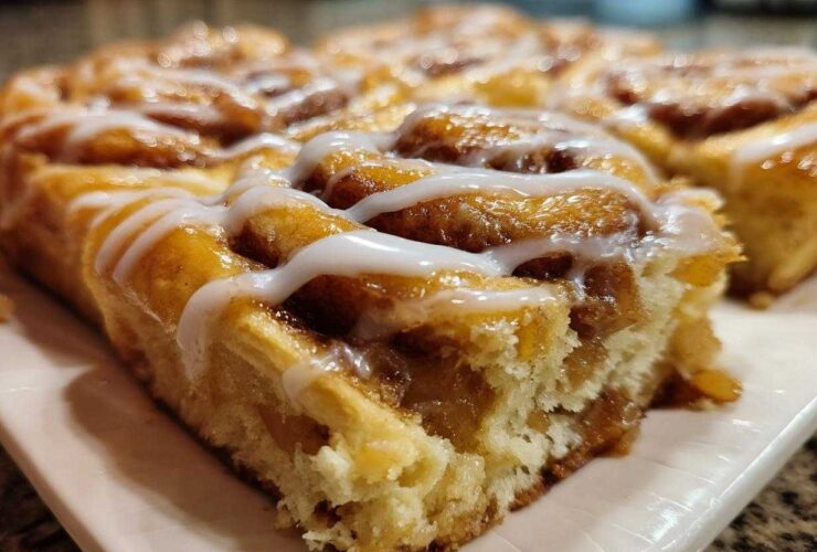 Close-up of a soft, gooey slice of cinnamon roll apple pie topped with white icing.