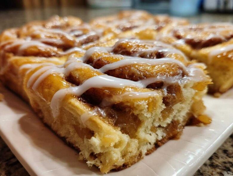 Close-up of a soft, gooey slice of cinnamon roll apple pie topped with white icing.