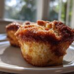 Close-up of a freshly baked french toast muffin topped with sparkling cinnamon sugar, sitting on a white plate.