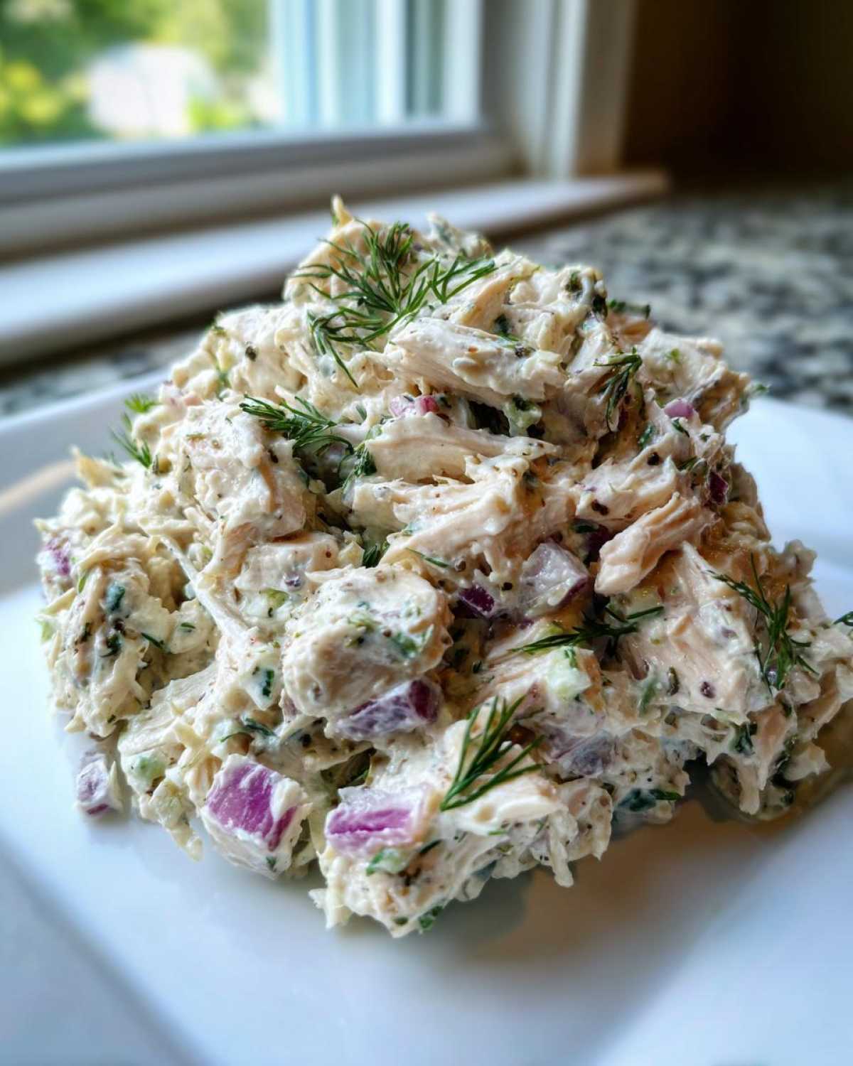 A scoop of creamy cottage cheese chicken salad mixed with red onion and topped with fresh dill.