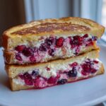 Two halves of creamy berry stuffed french toast stacked on a white plate, showing rich filling.