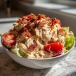 A bowl filled with creamy blt chicken salad, garnished with halved cherry tomatoes and crispy bacon bits.
