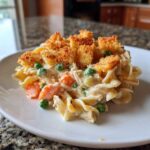 A serving of creamy chicken noodle casserole mixed with peas and carrots, topped with golden brown croutons.