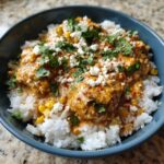Close-up of a delicious chicken rice bowl featuring creamy orange sauce, corn, crumbled white cheese, and fresh cilantro.