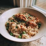 A close-up of creamy one pot chicken and rice mixed with bright green peas, topped with seared chicken pieces.