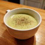 A close-up of creamy potato leek soup in a white mug, generously topped with freshly ground black pepper.