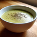 A white bowl filled with creamy potato leek soup, garnished with freshly ground black pepper.