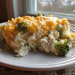 A serving of creamy rice casserole mixed with chicken and broccoli, topped with melted cheddar cheese.