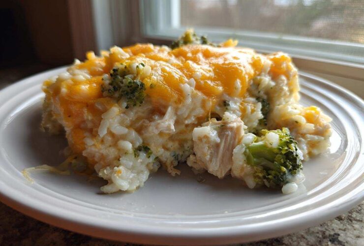 A serving of creamy rice casserole mixed with chicken and broccoli, topped with melted cheddar cheese.