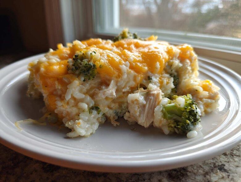 A serving of creamy rice casserole mixed with chicken and broccoli, topped with melted cheddar cheese.