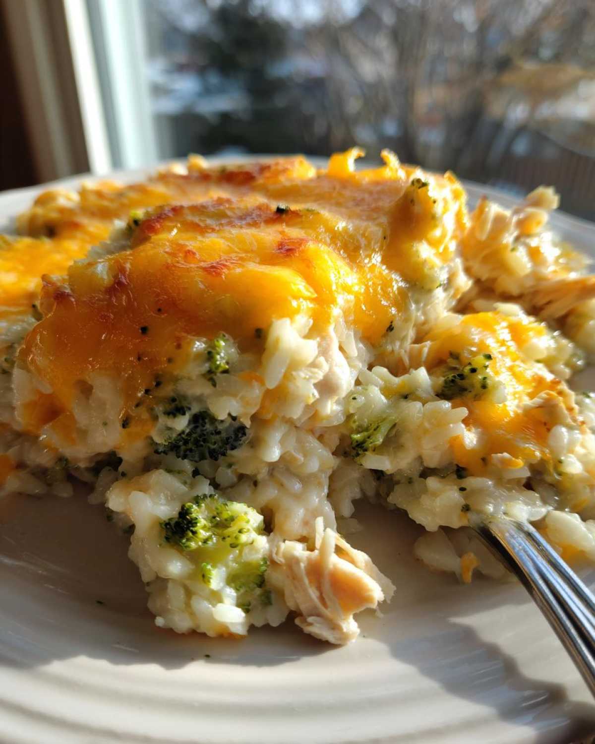 Close-up of a creamy rice casserole with chicken and broccoli, topped with melted, bubbly cheddar cheese.