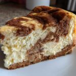 A close-up view of a thick slice of creamy snickerdoodle cheesecake with cinnamon swirls on a white plate.