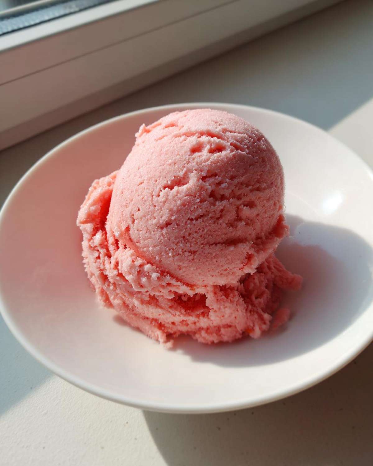 A single, perfectly scooped serving of pink strawberry ice cream in a white bowl.