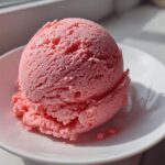 A perfectly scooped ball of bright pink strawberry ice cream sitting in a white bowl, catching sunlight.