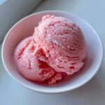 Two scoops of bright pink, creamy strawberry ice cream served in a small white bowl.