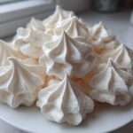 A pile of crisp, white meringue cookies piped into star shapes, displayed on a white plate.