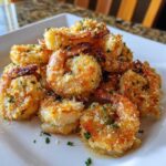 A pile of golden, crispy breaded air fryer shrimp garnished with parsley on a white square plate.