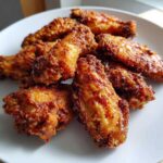 A close-up of several golden-brown, crispy baked chicken wings piled on a white plate.