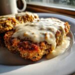 Close-up of crispy chicken fried steak smothered in creamy, peppered white gravy on a white plate.