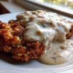 A close-up of crispy chicken fried steak smothered in rich, peppered white gravy.