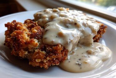 A close-up of crispy chicken fried steak smothered in rich, peppered white gravy.