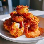 A pile of golden brown crispy coconut shrimp served with a side of orange dipping sauce, not ricotta dip.