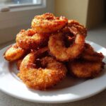 A tall stack of golden brown, crispy fried shrimp piled high on a white plate, ready to eat.