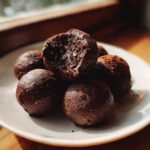 A pile of decadent, dark chocolate Oreo balls, one of which is bitten into, showing the rich interior.
