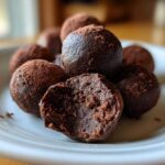 A pile of rich, dark chocolate Oreo balls dusted with cocoa powder, one is bitten open showing the dense interior.