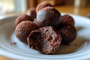 A pile of rich, dark chocolate Oreo balls dusted with cocoa powder, one is bitten open showing the dense interior.