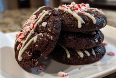 A stack of rich, fudgy double chocolate peppermint cookies drizzled with white chocolate and topped with crushed candy canes.