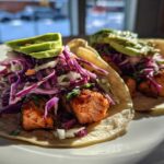 Two delicious salmon tacos topped with vibrant purple cabbage slaw and sliced avocado.
