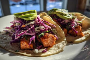 Two delicious salmon tacos topped with vibrant purple cabbage slaw and sliced avocado.