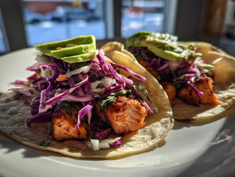 Two delicious salmon tacos topped with vibrant purple cabbage slaw and sliced avocado.