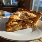 A close-up of a thick slice of apple pie recipe showing a flaky, sugared crust and rich cinnamon apple filling.