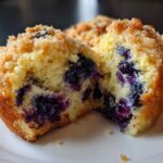 Close-up of a fluffy blueberry muffin cut in half, showing moist crumb and burst blueberries, topped with streusel.