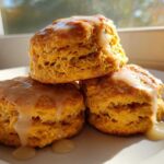 Three fluffy sweet potato biscuits stacked and drizzled with a vanilla glaze, sitting on a white plate.