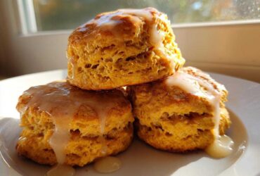 Three fluffy sweet potato biscuits stacked and drizzled with a vanilla glaze, sitting on a white plate.