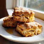 Three fluffy sweet potato biscuits stacked on a white plate, drizzled with a thick, light-colored glaze.
