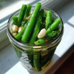 Close-up of bright green dilly beans packed tightly in a glass jar with garlic cloves and fresh dill.
