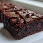 Close-up of a fudgy, dark chocolate black bean brownies slice topped with melted chocolate chips.