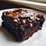 Close-up of a rich, fudgy square of black bean brownies topped with melted chocolate chips.